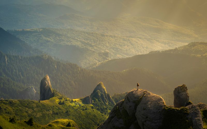 A lone walker looking out over a wide valley at sunrise