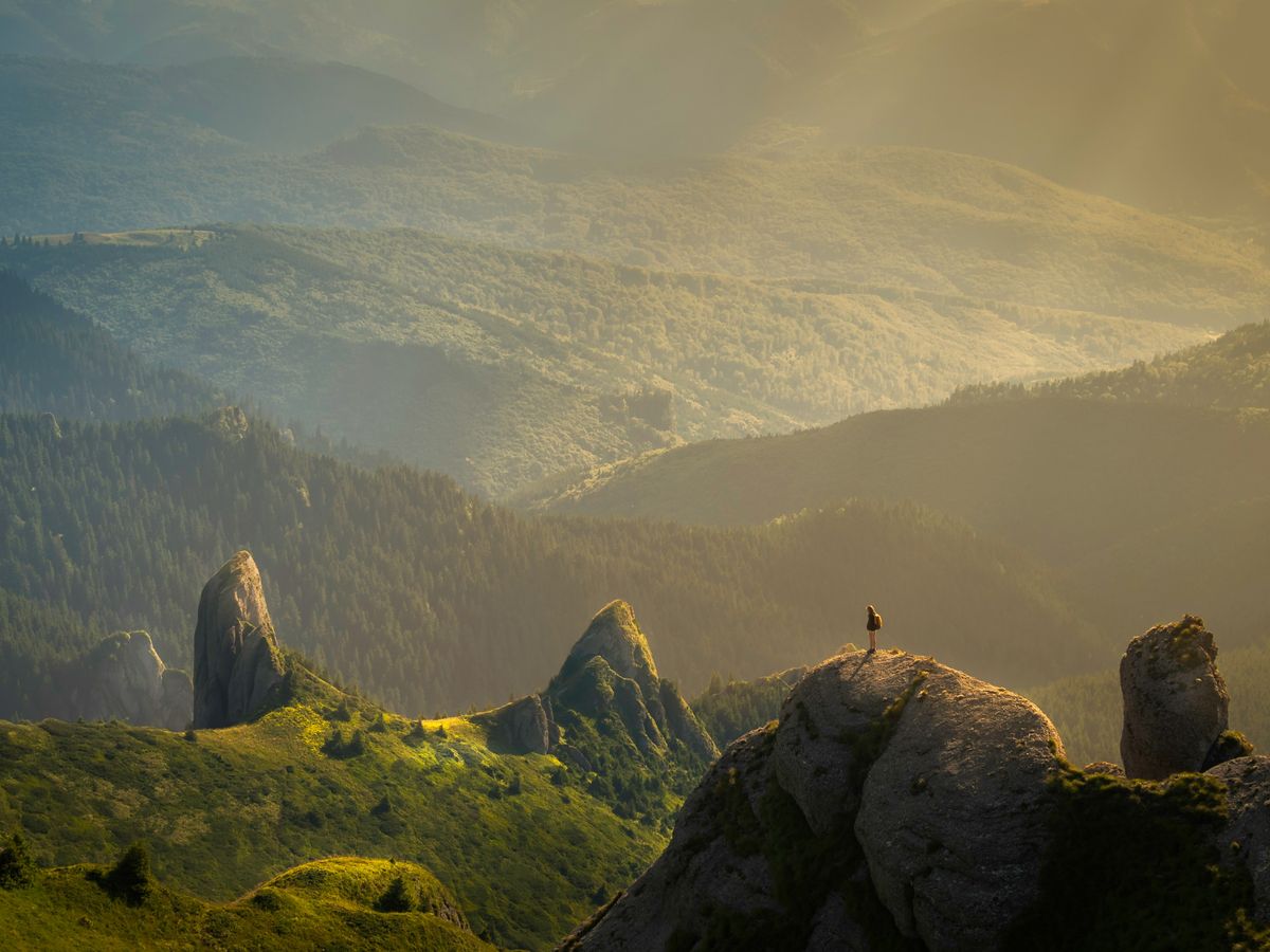 A lone walker standing on a rock, looking out over a wide valley at sunrise